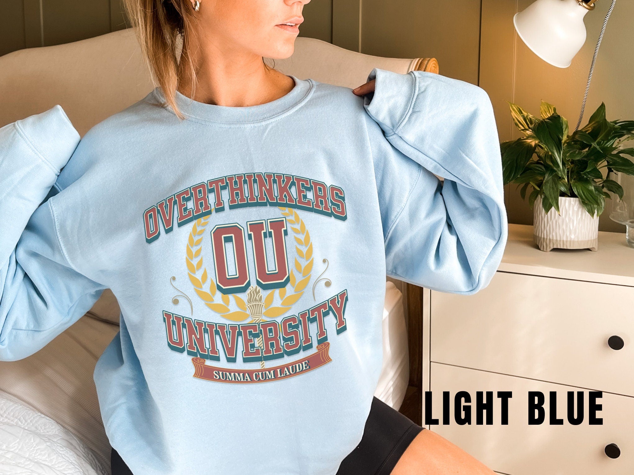 a woman sitting on a bed wearing a light blue sweatshirt