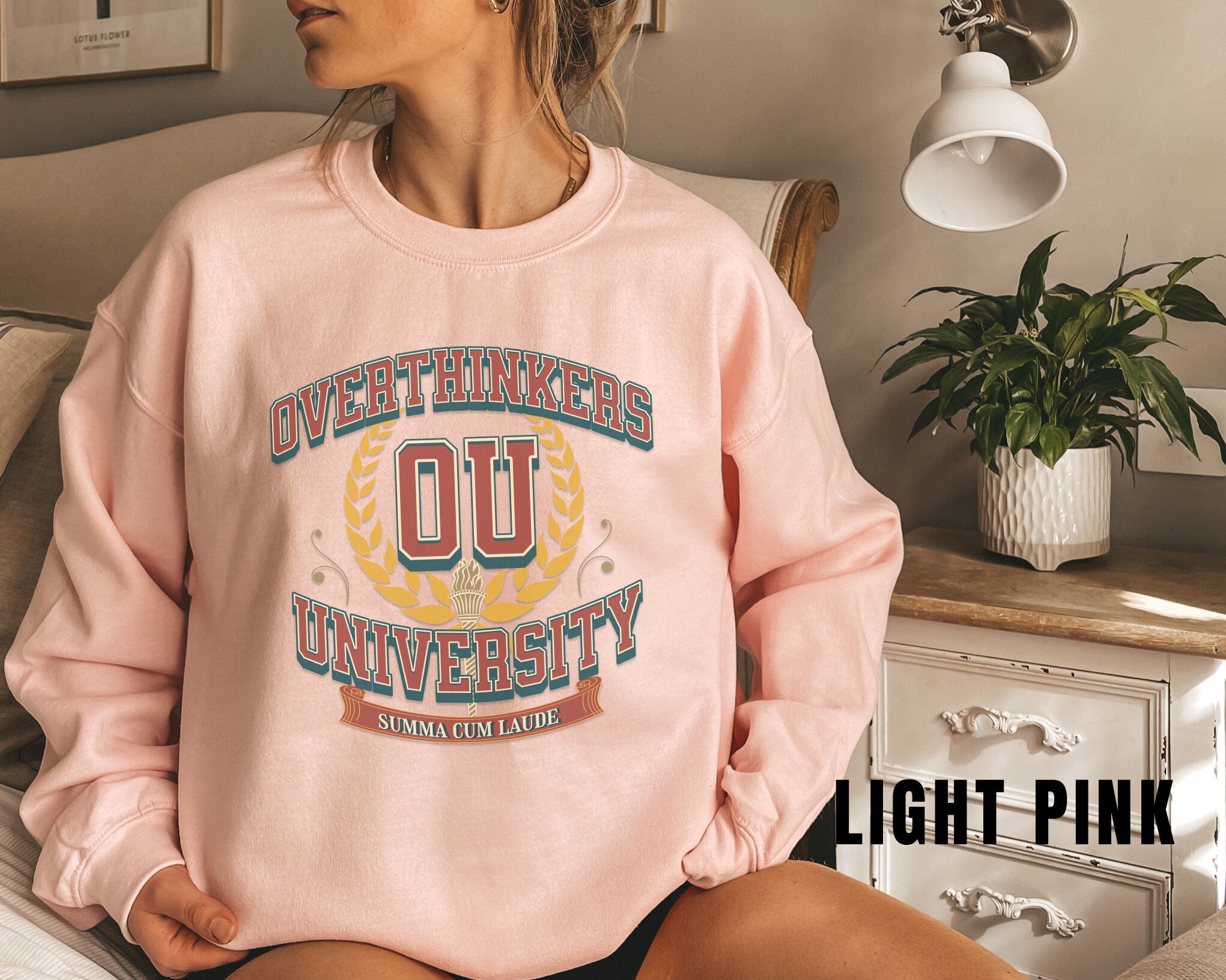 a woman sitting on a couch wearing a pink sweatshirt