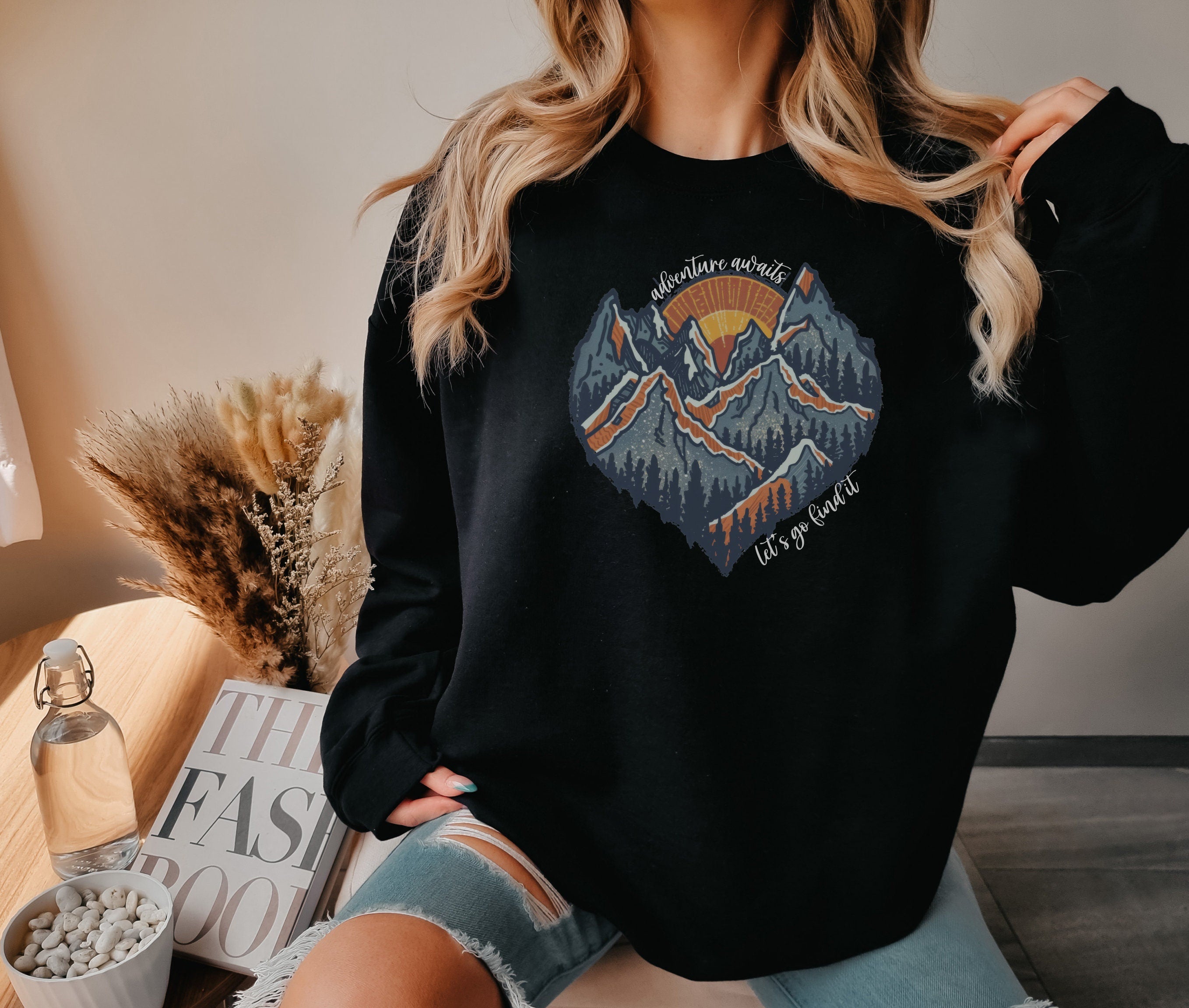 a woman wearing a black sweatshirt with a mountain scene on it