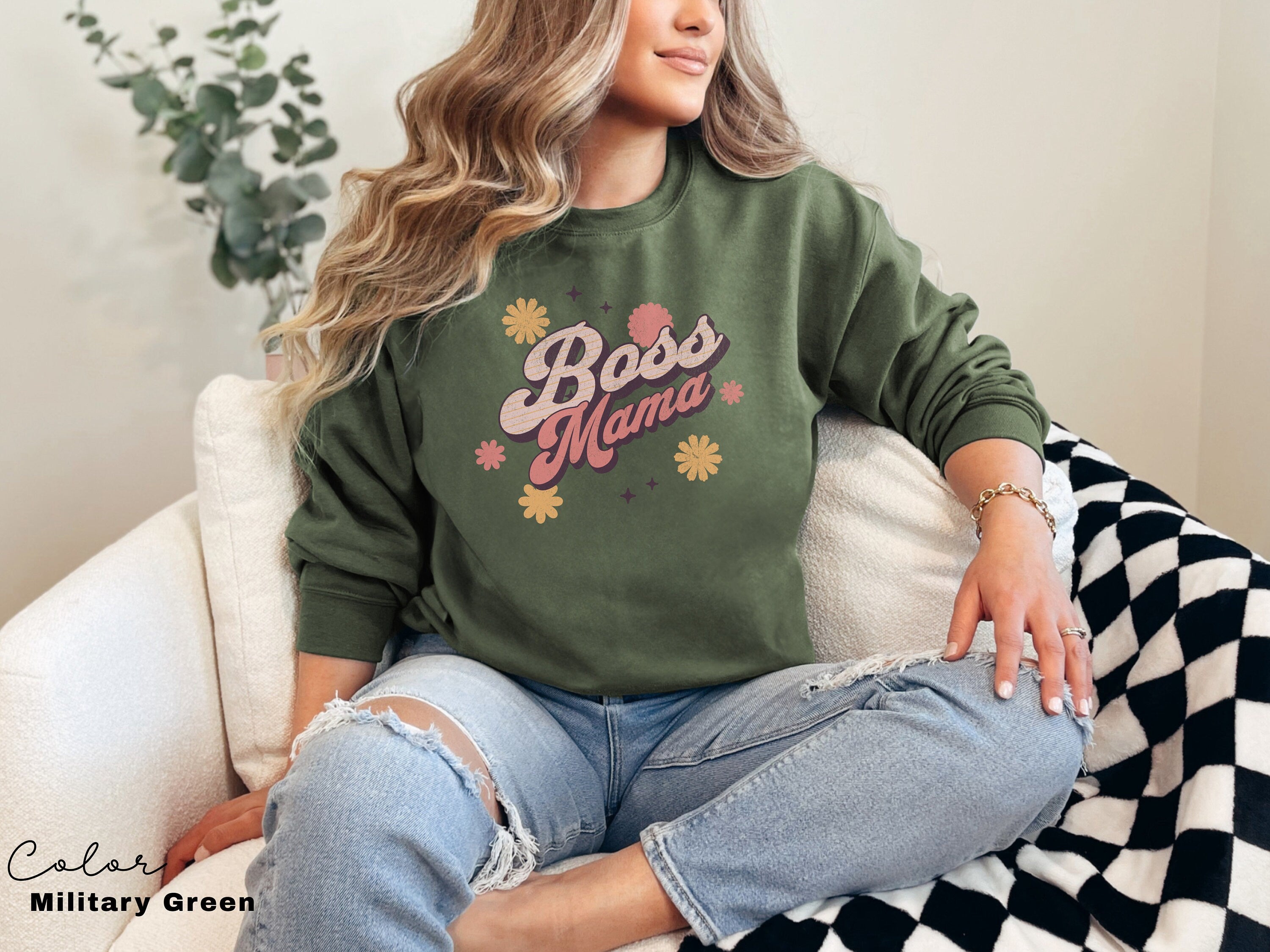 a woman sitting on a couch wearing a green boss mama sweatshirt
