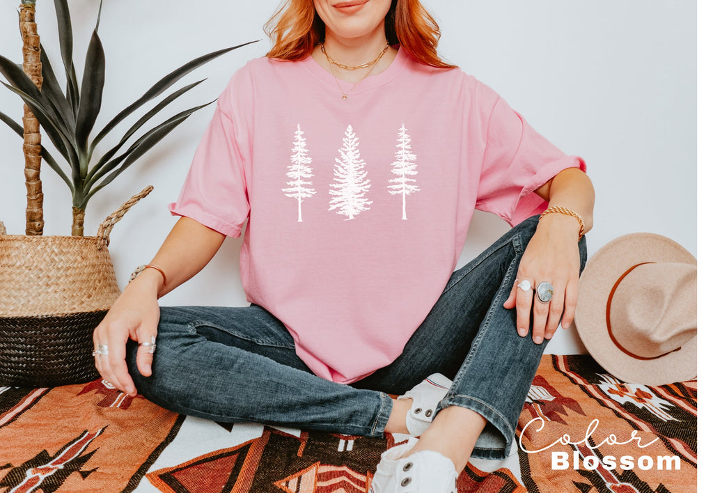 a woman sitting on the floor wearing a pink shirt with white trees on it