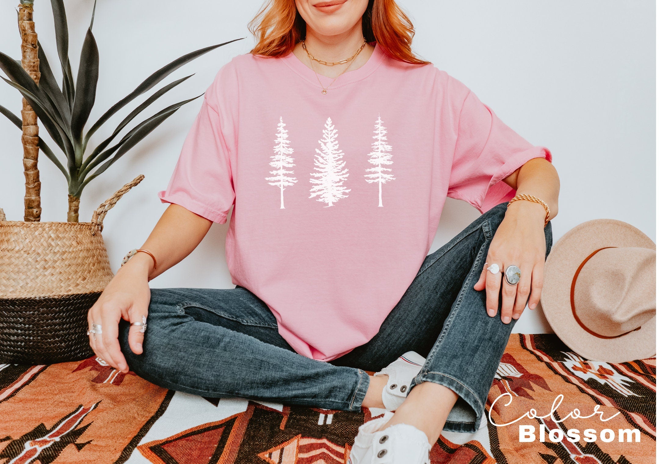 a woman sitting on the floor wearing a pink shirt with white trees on it