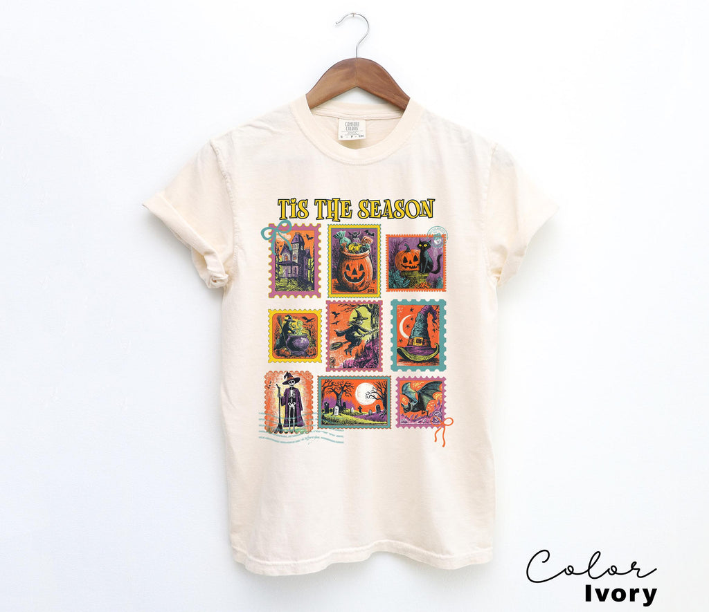A white t-shirt with a graphic design featuring a collection of Halloween-themed stamps.