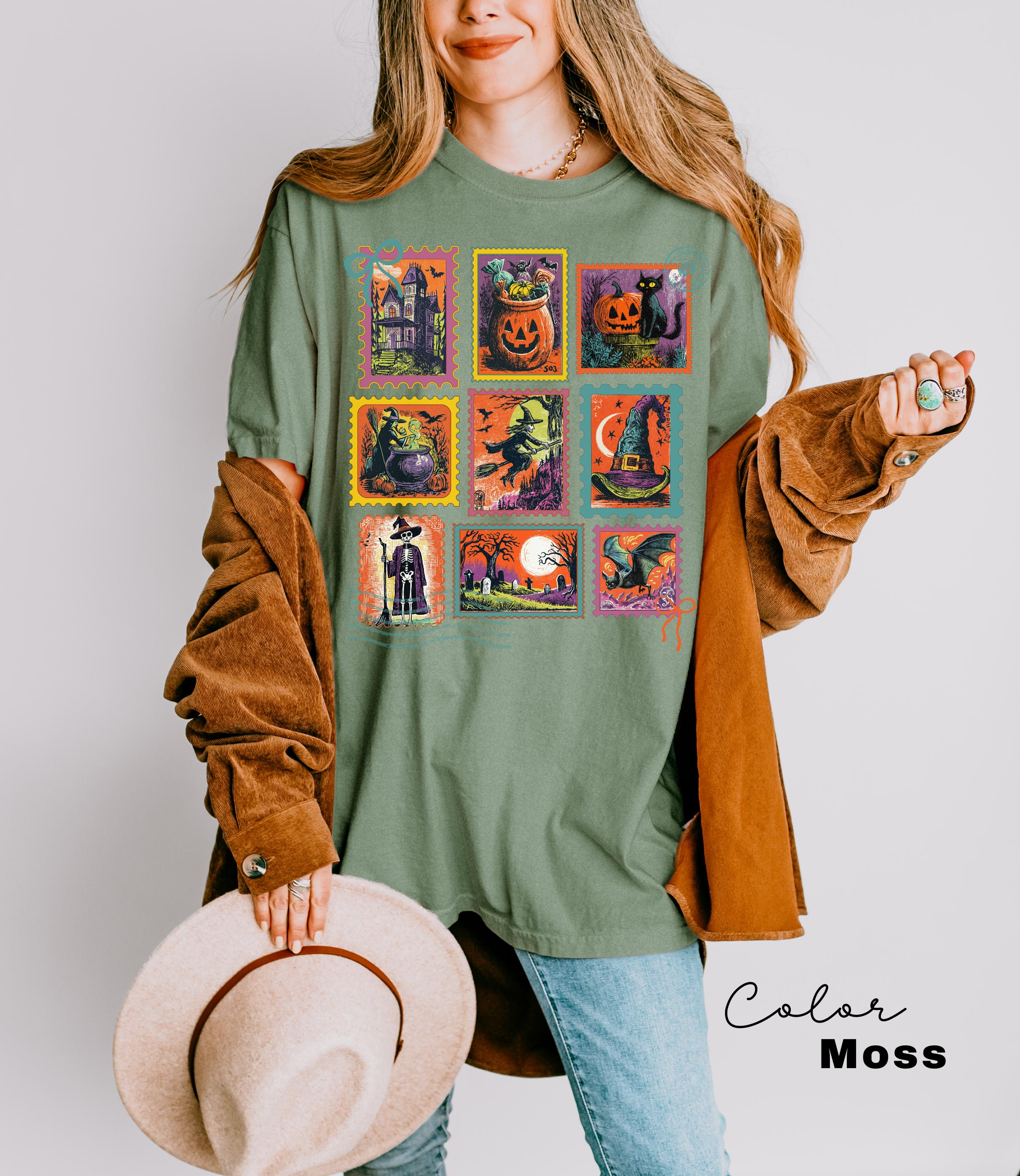 A woman wearing a green t-shirt with a collage of Halloween-themed illustrations, including a jack-o-lantern, witch, broomstick, and other spooky scenes. She is holding a beige hat and wearing a brown jacket.