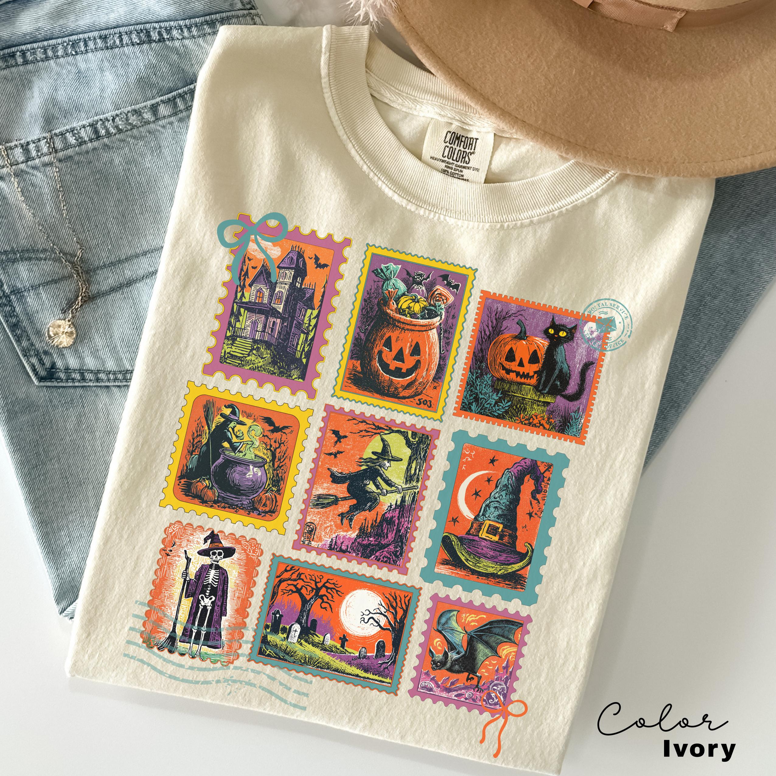A white t-shirt with a colorful design of Halloween-themed stamps, including a castle, pumpkin, witch, cat, and other spooky and festive illustrations.