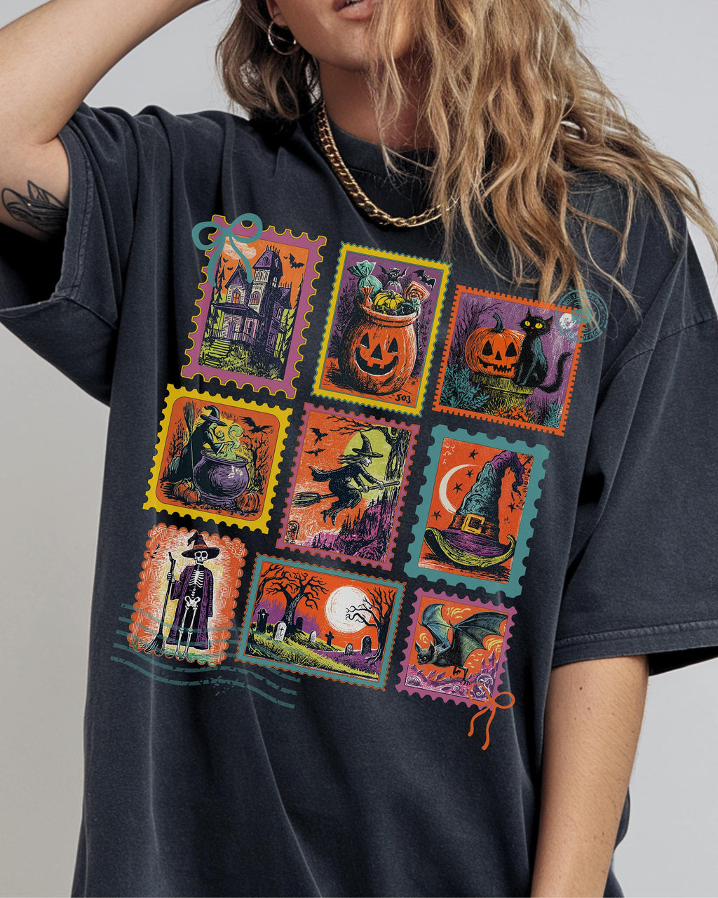 A woman wearing a black t-shirt with a graphic design featuring various Halloween-themed illustrations, including a jack-o-lantern, a witch's broomstick, a witch's cauldron, a witch's hat, a skeleton, a cemetery, a full moon, and a bat.