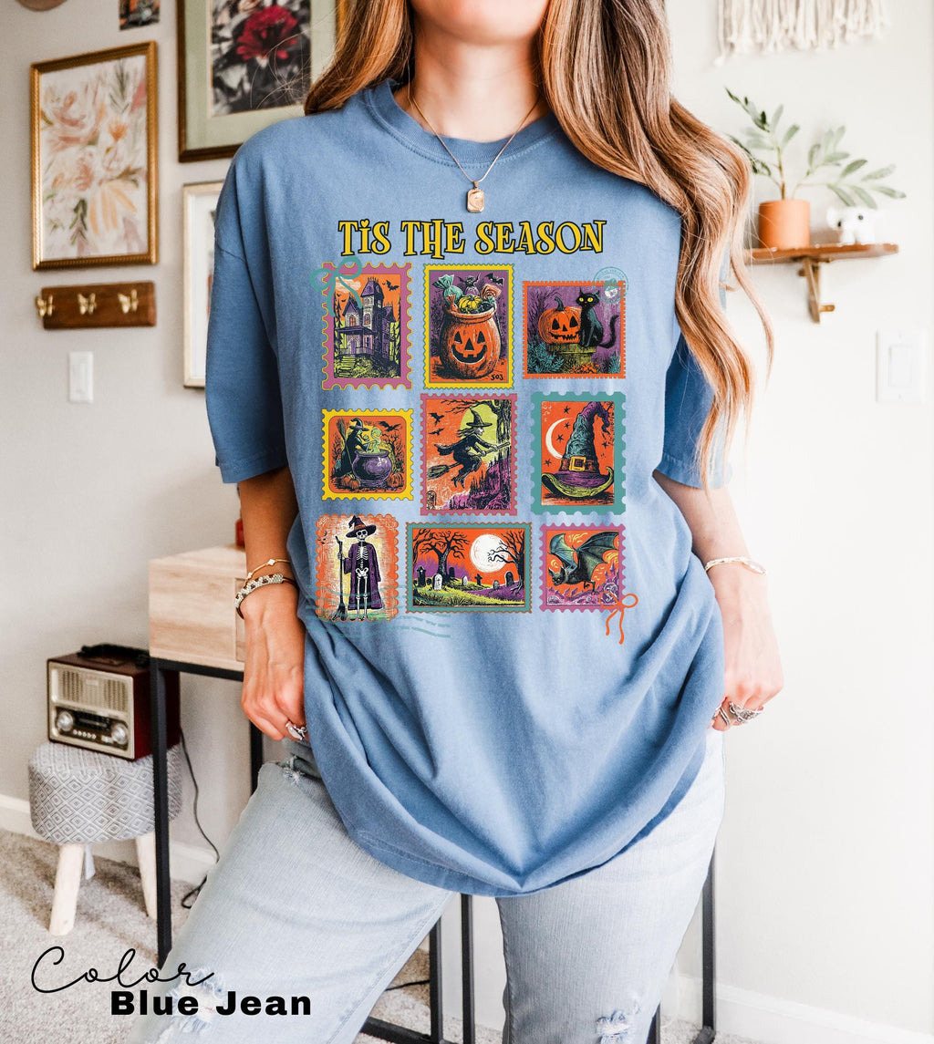 A woman wearing a blue t-shirt with a graphic design of various Halloween-themed illustrations, including pumpkins, bats, and other spooky elements.