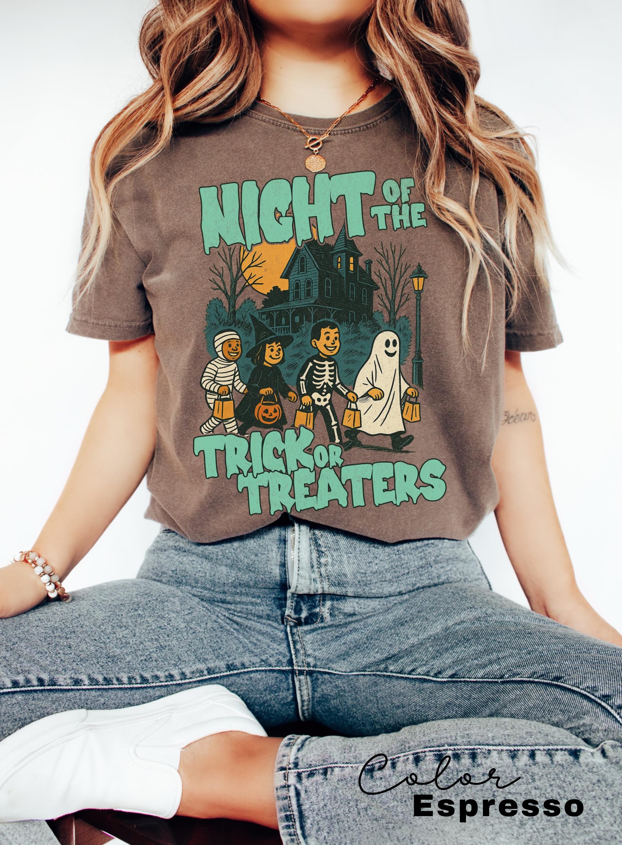 A woman wearing a t-shirt with a Halloween-themed graphic design, including a skeleton, ghost, and trick or treaters.