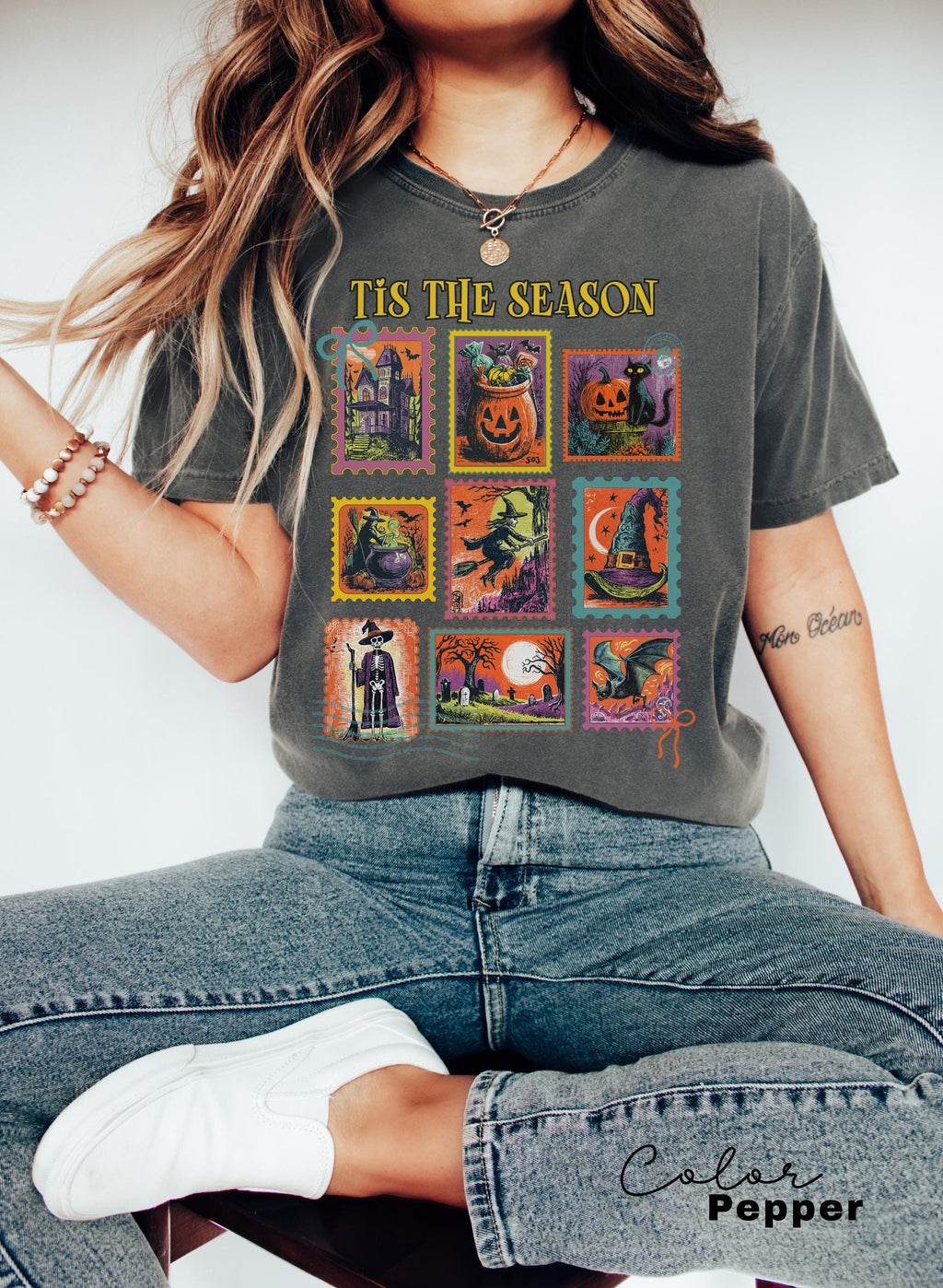 A woman wearing a gray t-shirt with a graphic design of Halloween-themed illustrations, including pumpkins, bats, and other spooky elements.