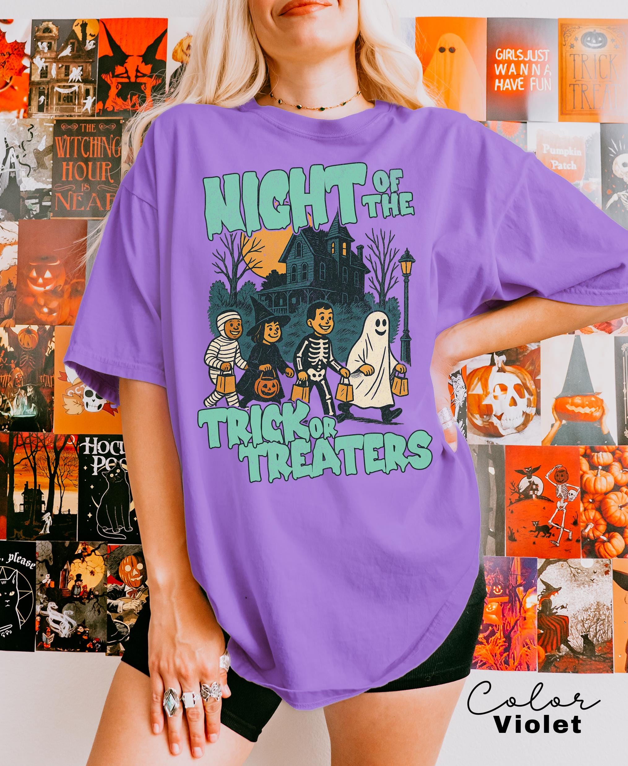 A woman wearing a purple t-shirt with a Halloween-themed graphic design, including a skeleton, ghost, and trick or treaters.